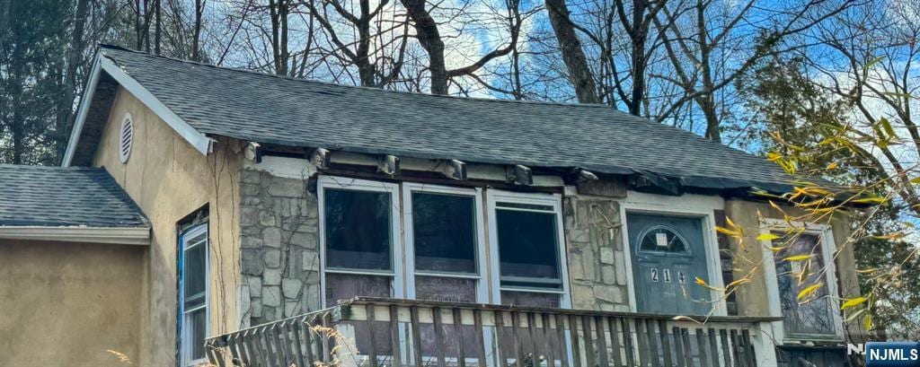 exterior space with stone siding and a shingled roof