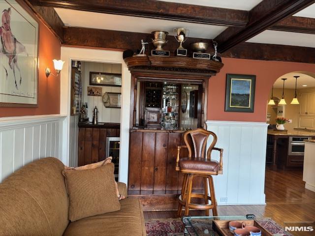 bar featuring a wainscoted wall, beam ceiling, and wet bar