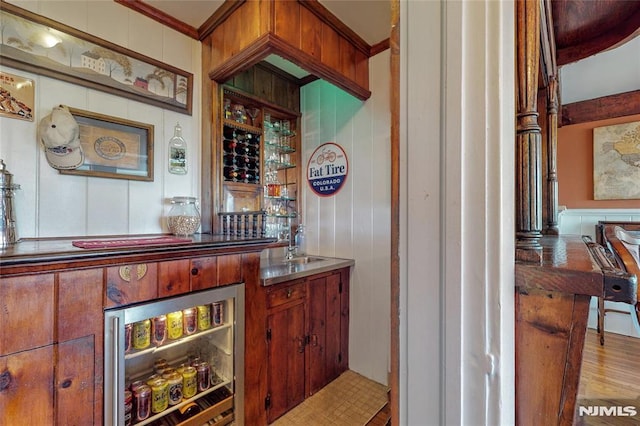 bar featuring wine cooler, a bar, crown molding, and wood finished floors