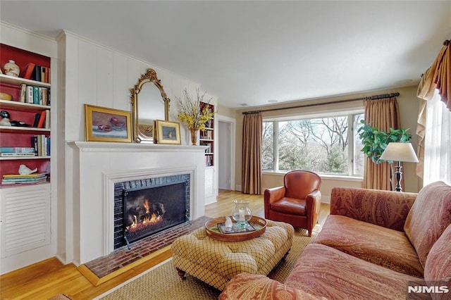 living room with built in shelves, wood finished floors, and a warm lit fireplace