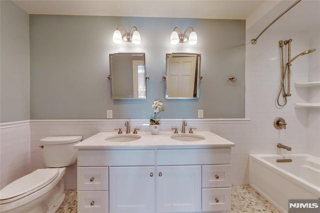 full bath with tile walls, toilet, wainscoting, and a sink