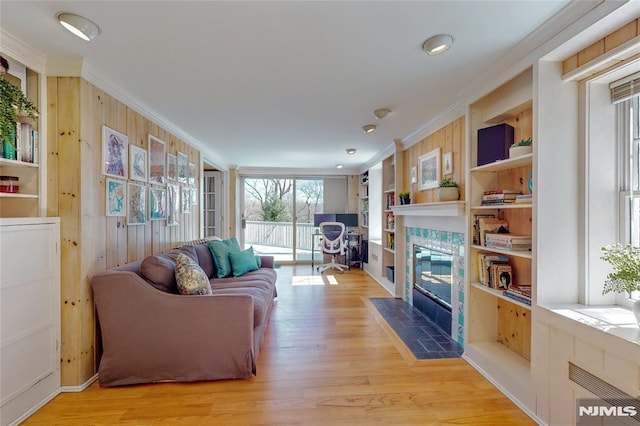 living room featuring light wood finished floors, wood walls, crown molding, and a tile fireplace