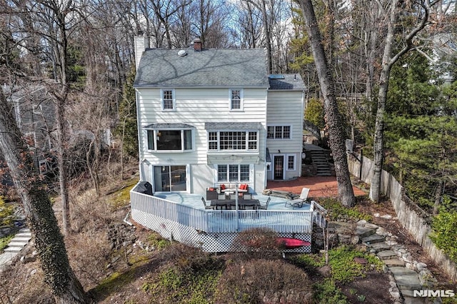 rear view of house featuring a wooden deck, a chimney, and fence