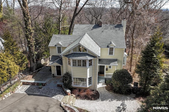 view of front facade featuring aphalt driveway, fence, roof with shingles, and a chimney