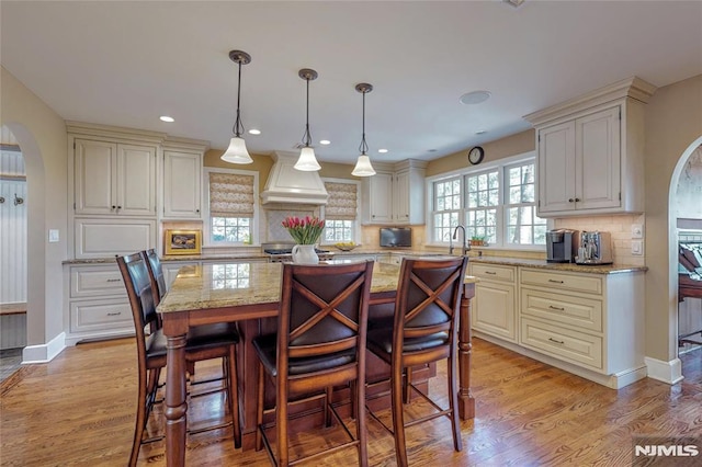 kitchen with arched walkways, custom exhaust hood, light wood-style flooring, and light stone countertops