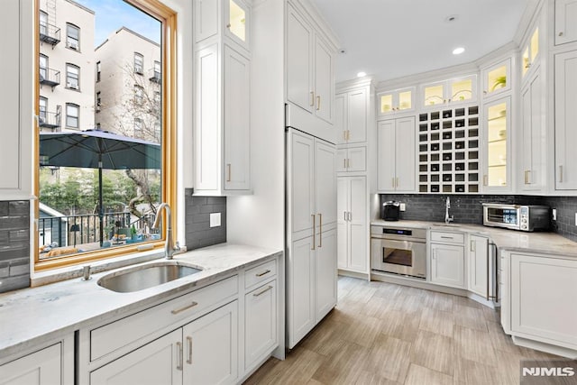 kitchen with stainless steel oven, white cabinetry, backsplash, and a sink