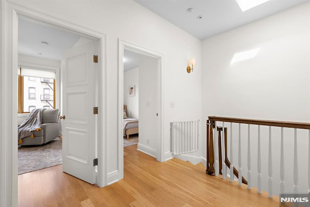 corridor with a skylight, an upstairs landing, light wood-style floors, and baseboards