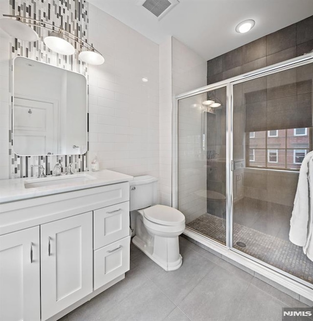 bathroom featuring tile patterned flooring, visible vents, a shower stall, vanity, and tile walls