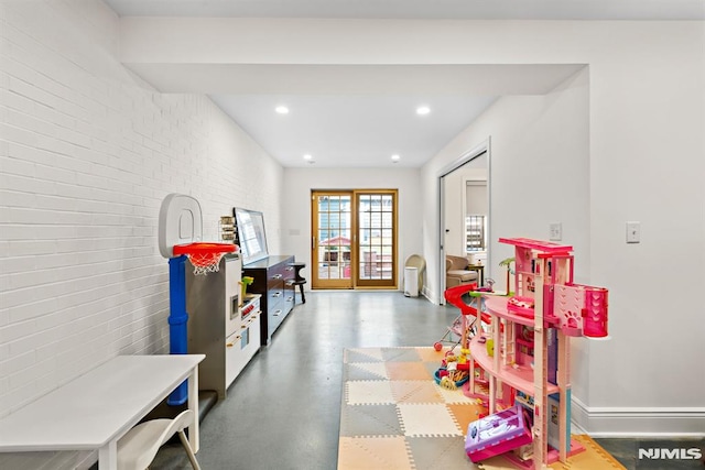 rec room featuring recessed lighting, baseboards, finished concrete flooring, and brick wall