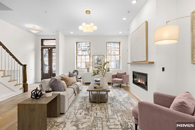 living area with light wood-type flooring, a glass covered fireplace, recessed lighting, baseboards, and stairs