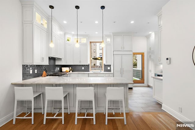 kitchen with a breakfast bar, white cabinetry, a peninsula, decorative backsplash, and hanging light fixtures