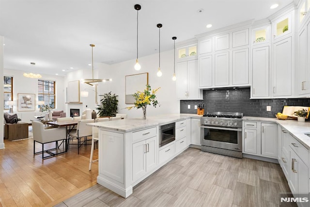 kitchen featuring stainless steel range, tasteful backsplash, white cabinetry, a lit fireplace, and a peninsula