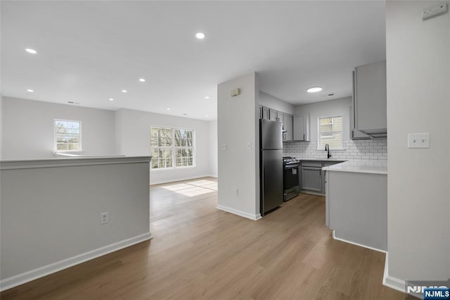 kitchen featuring backsplash, gray cabinetry, open floor plan, freestanding refrigerator, and range