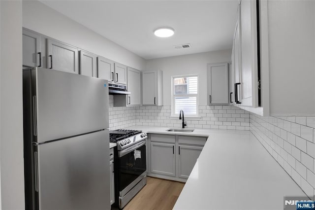 kitchen featuring visible vents, a sink, under cabinet range hood, appliances with stainless steel finishes, and light countertops