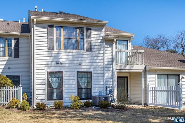 view of front of home featuring central air condition unit, a shingled roof, a balcony, and fence