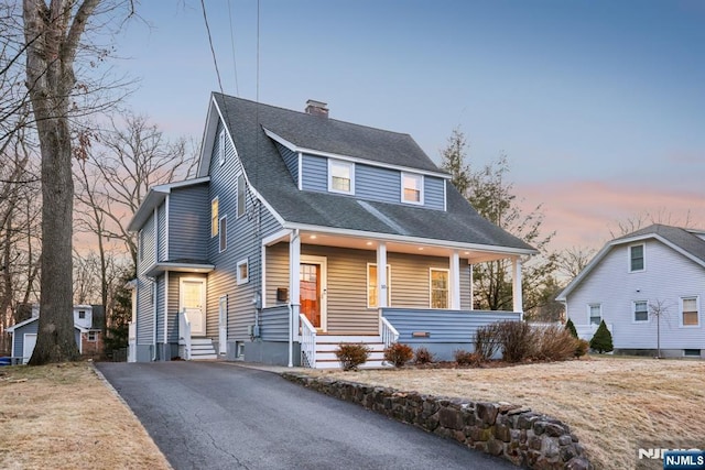 view of front of home with a porch, driveway, roof with shingles, and a chimney