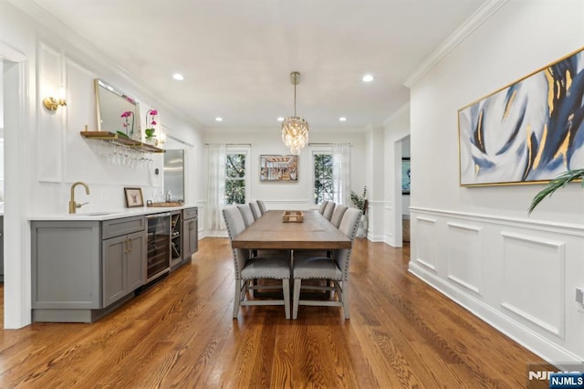 dining room with beverage cooler, ornamental molding, wet bar, and wood finished floors