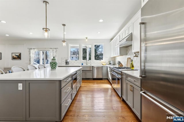 kitchen featuring gray cabinets, under cabinet range hood, light countertops, decorative backsplash, and high end appliances