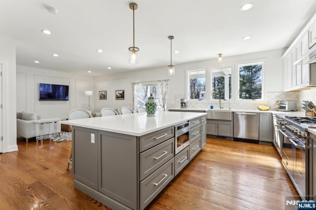 kitchen with a breakfast bar area, gray cabinets, a sink, decorative backsplash, and appliances with stainless steel finishes