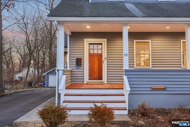 exterior entry at dusk with aphalt driveway and a shingled roof