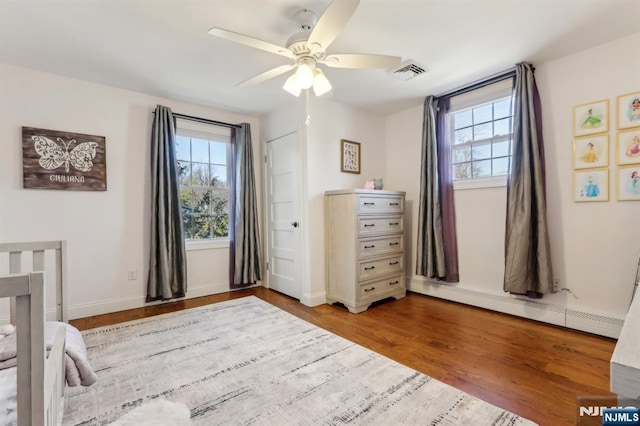 bedroom featuring a baseboard heating unit, multiple windows, wood finished floors, and visible vents