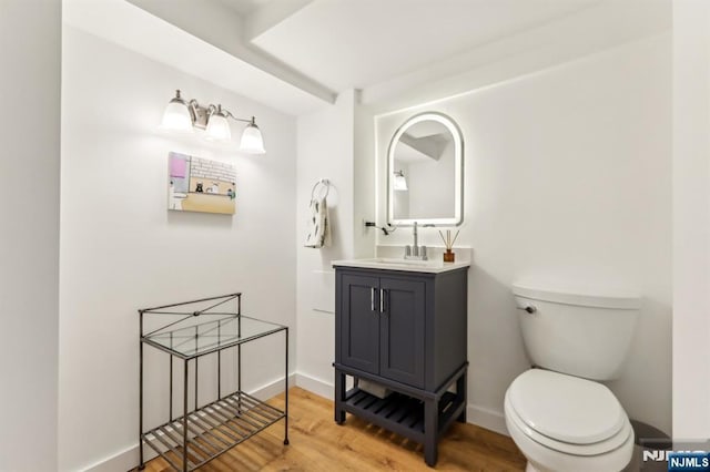 half bathroom featuring vanity, toilet, wood finished floors, and baseboards