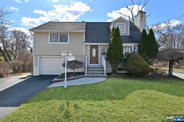 split level home featuring aphalt driveway, a shingled roof, a front yard, an attached garage, and a chimney