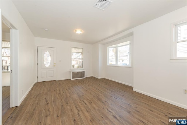 foyer entrance with radiator, wood finished floors, visible vents, and plenty of natural light