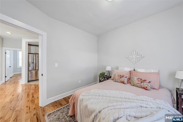 bedroom featuring light wood finished floors, baseboards, and stainless steel fridge with ice dispenser