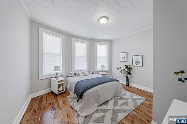 bedroom with baseboards, wood finished floors, and ornamental molding