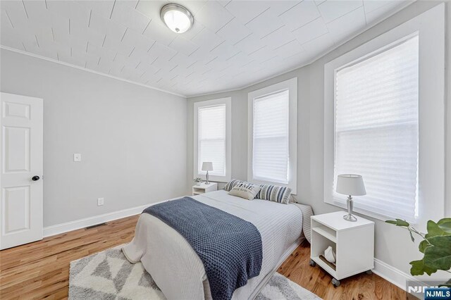 bedroom with crown molding, wood finished floors, and baseboards