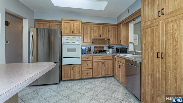 kitchen with a skylight, a sink, stainless steel appliances, light countertops, and a warming drawer