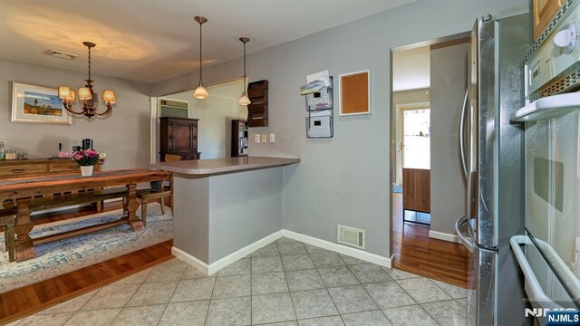 kitchen featuring visible vents, a chandelier, pendant lighting, freestanding refrigerator, and light tile patterned flooring