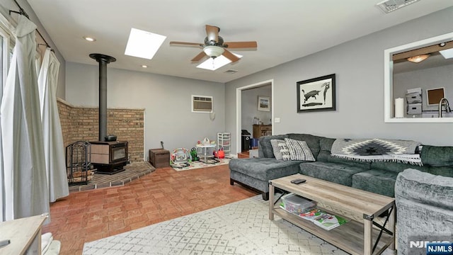 living area featuring a ceiling fan, visible vents, a wood stove, a skylight, and a wall mounted air conditioner