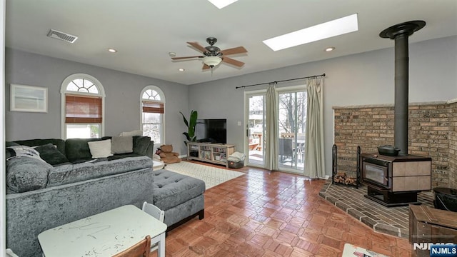 living area with visible vents, plenty of natural light, a wood stove, and ceiling fan