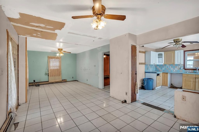 empty room with light tile patterned flooring, a ceiling fan, baseboard heating, and a sink