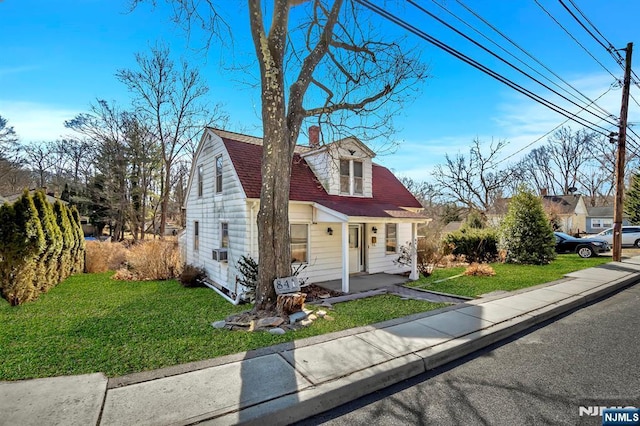 view of front facade with a chimney, a gambrel roof, roof with shingles, and a front yard