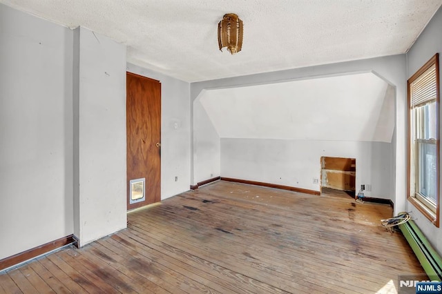 additional living space featuring a textured ceiling, hardwood / wood-style floors, baseboards, baseboard heating, and vaulted ceiling