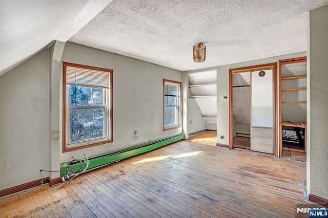 unfurnished bedroom featuring multiple closets, a textured ceiling, wood-type flooring, baseboards, and baseboard heating