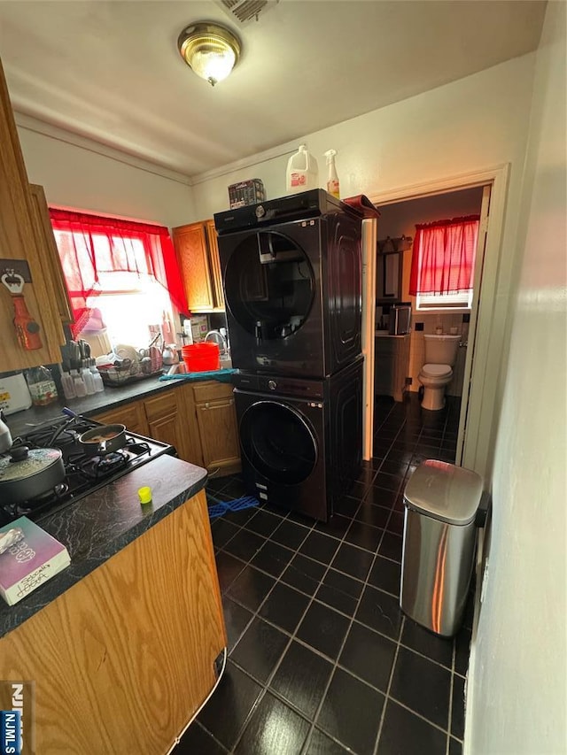 kitchen featuring cooktop, dark tile patterned flooring, stacked washer / dryer, and dark countertops