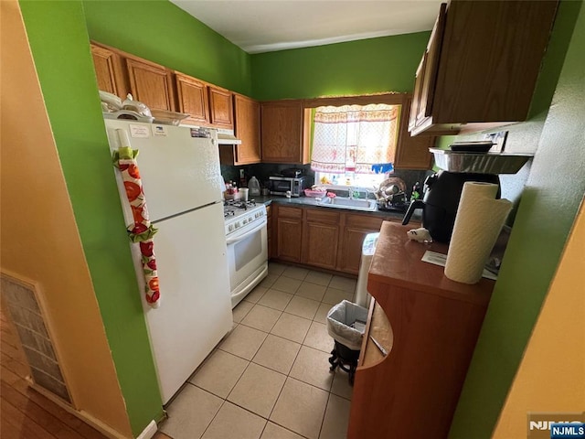 kitchen with visible vents, under cabinet range hood, dark countertops, white appliances, and light tile patterned floors