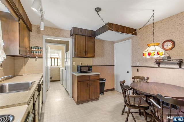 kitchen featuring light floors, wallpapered walls, a sink, light countertops, and black microwave