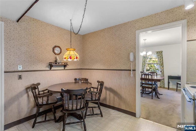 dining area featuring a notable chandelier, a wainscoted wall, light floors, and wallpapered walls