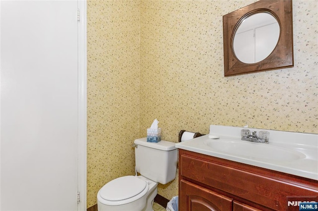 bathroom with toilet, wallpapered walls, and vanity