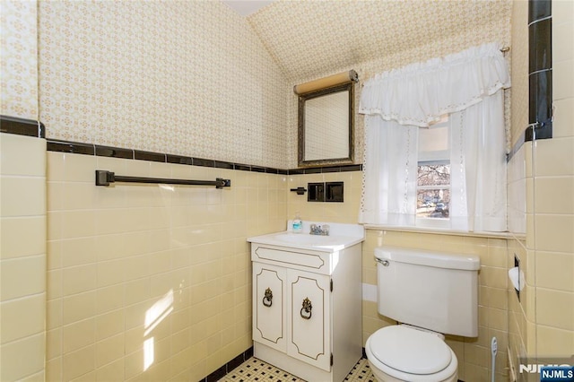 bathroom with a wainscoted wall, toilet, wallpapered walls, and tile walls