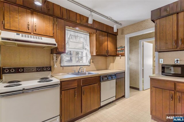 kitchen featuring white appliances, light floors, wallpapered walls, a sink, and under cabinet range hood