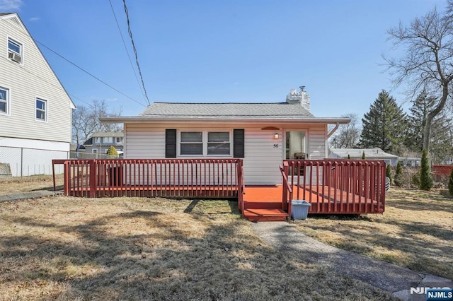 view of front facade featuring a deck, a front yard, fence, and a chimney