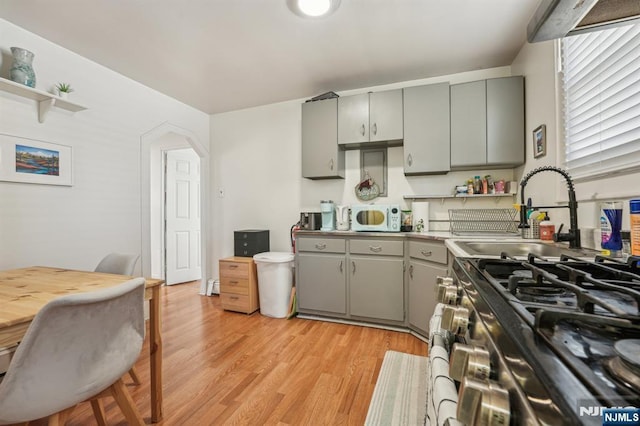 kitchen featuring a sink, white microwave, light wood-style floors, and gray cabinetry