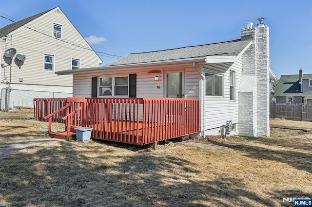 view of front of property featuring a front lawn, fence, roof with shingles, a chimney, and a deck