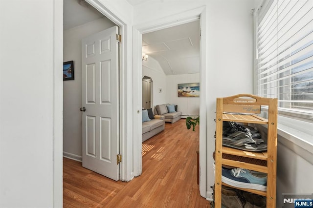 hallway with arched walkways, light wood-style flooring, and vaulted ceiling